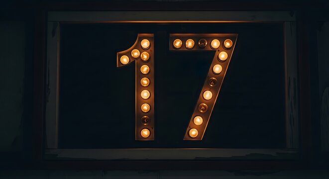 Illuminated number seventeen with retro-style light bulbs creating a warm glow in a dark, framed display for an anniversary or event