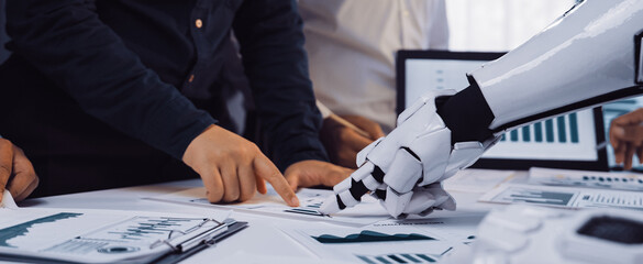 A team of business professionals engages with an advanced robotic arm, analyzing data charts and reports in a modern office setting, showcasing innovation and collaboration.Noogenesis