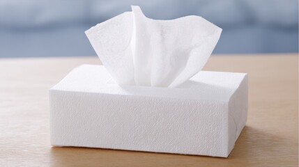 A tissue box is placed on a wooden surface. The box is empty and the tissue inside is white