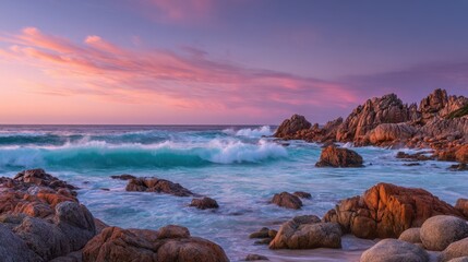 The scene captures waves splashing over rocky formations as the sky glows with sunset hues. Soft clouds drift above enhancing the tranquil coastal atmosphere.