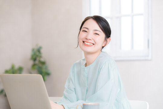 笑顔でパソコン作業をする女性の在宅ワークシーン　カメラ目線