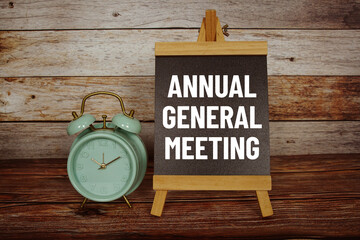 AGM Annual General Meeting text on easel blackboard with alarm clock on wooden background