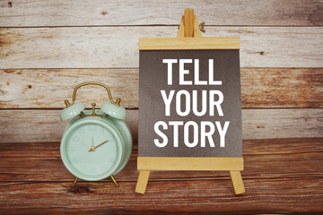 Tell Your Story text on easel blackboard with alarm clock on wooden background