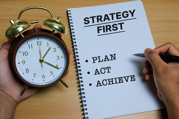 A classic alarm clock beside a notebook with the words STRATEGY FIRST, PLAN, ACT, and ACHIEVE, symbolizing concept time management, productivity, business strategy, and effective goal execution