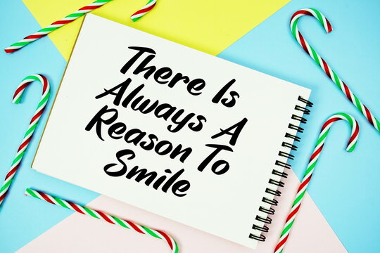 There Is Always A Reason To Smile message of season holidays written on notepad with candy cane decoration on pastel background