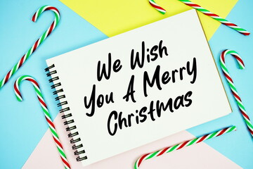 Obraz premium We Wish You A Merry Christmas message of season holidays written on notepad with candy cane decoration on pastel background