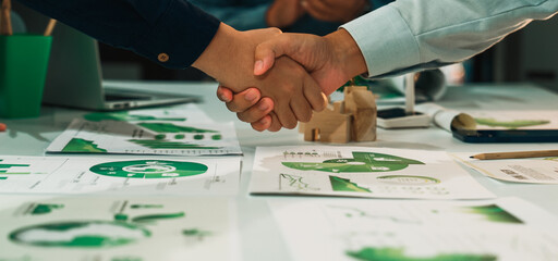 A close-up of hands shaking over business strategy documents featuring graphs and charts,...