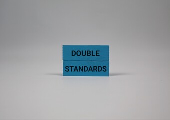 blue wooden blocks with the words “DOUBLE STANDARDS” stand against a white background, symbolizing unfair judgment, inequality, and inconsistent expectations in society or relationships.
