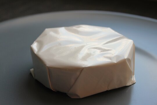 Sealed brie style cheese in glossy wrapSmall round brie style cheese sealed in glossy food grade wrap on a plate. Neutral product image for packaging mockups and store listings.