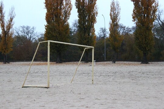 Rusty football goal posts installed on a sandy riverside field. Autumn trees and overcast sky. - Powered by Adobe