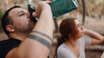 Man drinking water bottle, refreshing during nature hike with woman