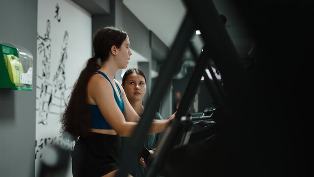 Personal trainer guiding young woman on fitness machine in modern gym