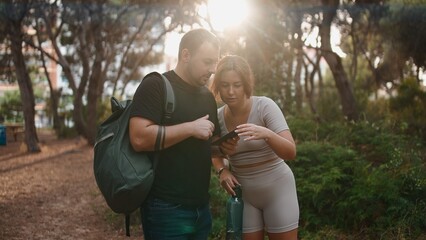 Couple hiking through forest checking smartphone for navigation or social media