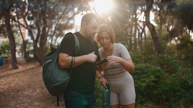 Couple hiking through forest checking smartphone for navigation or social media