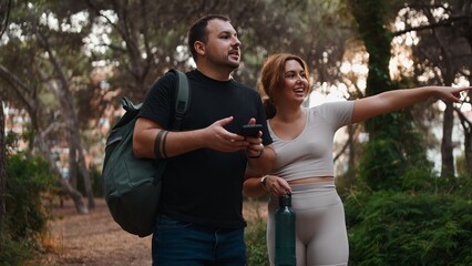 Couple exploring nature, man holding phone and woman pointing direction