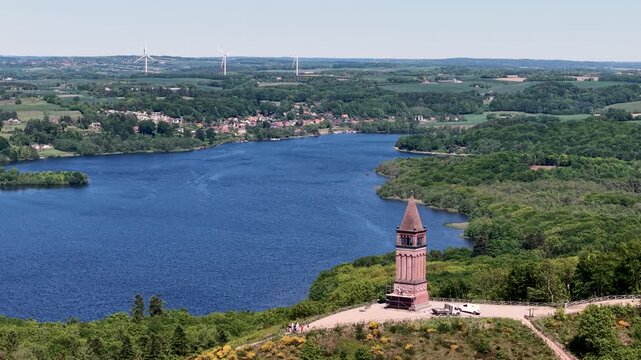 A drone captures the Himmelbjerget tower perched on a hill above a deep blue lake, surrounded by lush forests in Denmark.