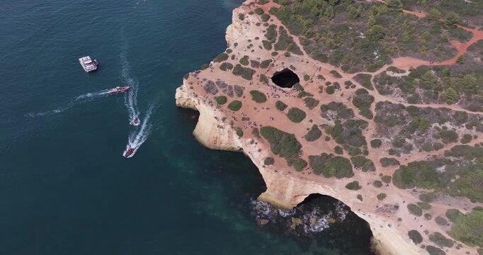 Aerial drone view of the Benagil Sea Cave and Atlantic Ocean coastline in Algarve, Portugal, Europe. Multiple tour boats crossing paths, concept shoot on mass tourism, preservation and overtourism
