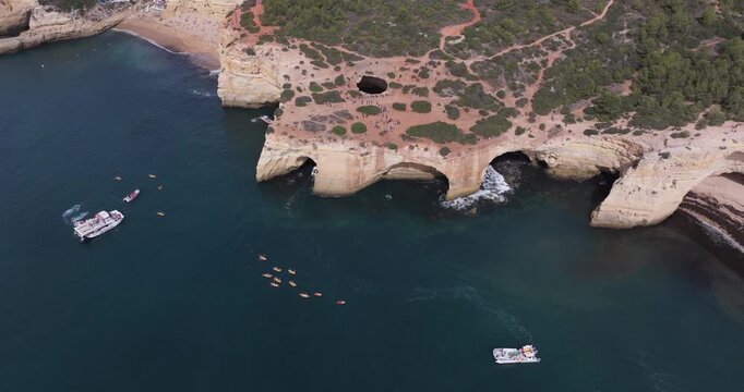 Aerial drone view of the Benagil Sea Cave and Atlantic Ocean coastline in Benagil, Algarve, Portugal, Europe. Boats, kayaks and people sightseeing