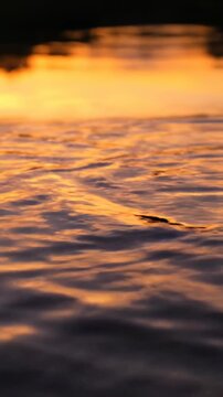 Beautiful slow motion abstract shot of gentle water ripples on a reflective pond surface creating distorted mirror images of warm golden hour sky colors soft focus, ripple effect, dreamy