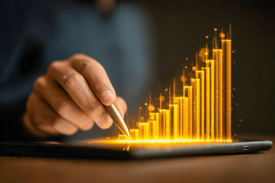 Person using a stylus on tablet with glowing golden rising bar graph representing business growth and successful digital data analysis concept - Powered by Adobe