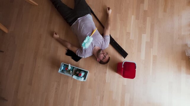 A tired man lying on the floor after cleaning, while a pet walks by, showing the mess and effort pets can cause.
