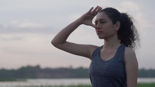 A woman performing pranayama breathing exercise outdoors near a river during peaceful sunrise