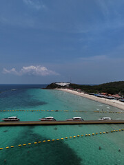 Obraz premium Aerial drone view of Samae Beach (Hat Samae) on Koh Larn (Coral Island), Pattaya, Thailand. The image captures long floating pontoon pier extending into the sea, lined with speedboats.