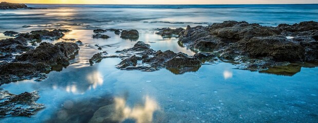 High resolution color panoramic long exposure landscape image of a beautiful sunset on the beach with natural rocks and cloud reflections in the water- Israel
