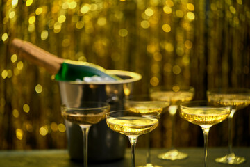 Bottle of champagne in a bucket with ice and glasses on blurred golden stylish background. Space for text. © Igor Dudchak