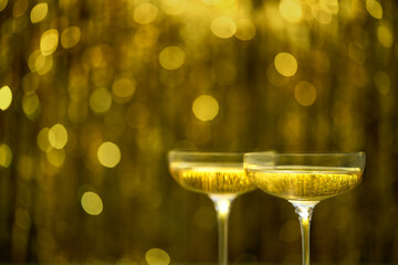 Two coupe glasses of champagne on golden bokeh background, selective focus.