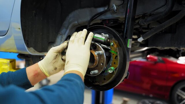 Mechanic in protective gloves repairs wheel hub and disk brakes on car, car is lifted . Various devices in a repair shop