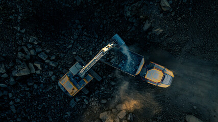Overhead view of an excavator loading rock onto a truck for crushing at a gravel quarry.