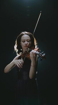 female musician with violin reading sheet notes on music stand, elegant woman playing violin under warm stage light, artistic creative concept of beauty inspiration and self expression, vertical frame