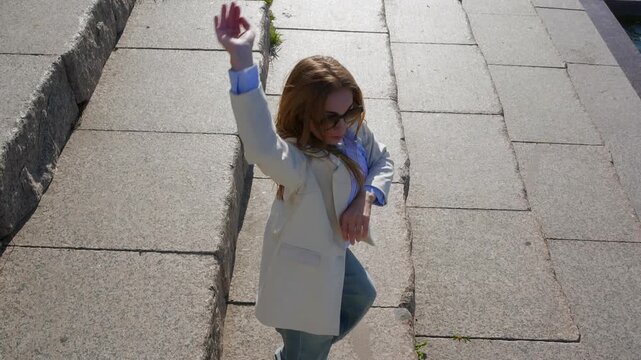 Young woman in loose jeans and light blazer dances contemporary modern dace energetically on outdoor granite steps, sunlight and shadows defining the mood.