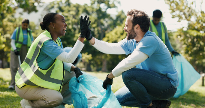 High five, volunteering and people in park, cleaning and support with teamwork. Outdoor, man and woman with trash bag, gesture and motivation with collaboration, eco friendly campaign and NGO charity