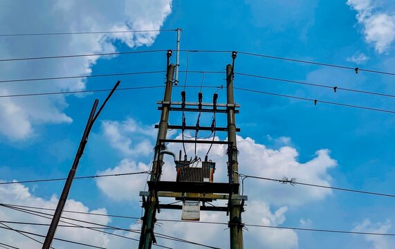 Electrical pole standing in a partly cloudy sky equipped with a transformer, some cables running horizontally. Insulators to support cables, the overall arrangement functions to distribute electricity