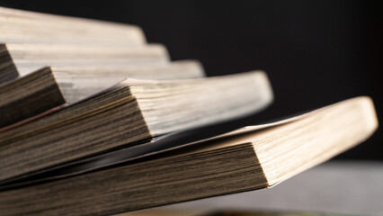 Close-up of angled paperback books with layered pages catching warm light, creating a soft abstract pattern suitable for themes of reading, study, or printed media textures.