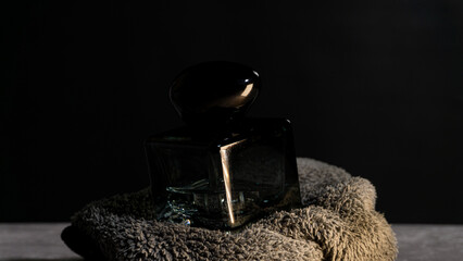 Dark, moody shot of a glass perfume bottle resting on textured fabric, highlighting reflections and luxury tones suitable for beauty, fragrance, elegance, or product styling.
