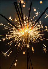 Close-up, vertical shot of a bundle of lit sparklers exploding outward in bright, golden light trails.