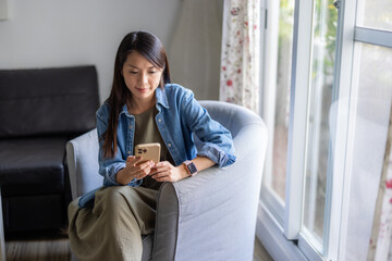 Woman using smartphone while relaxing at home on sofa