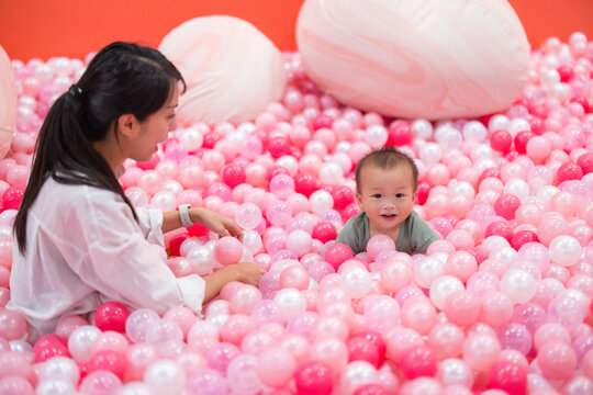 Mom enjoying ball pit play with little baby indoors
