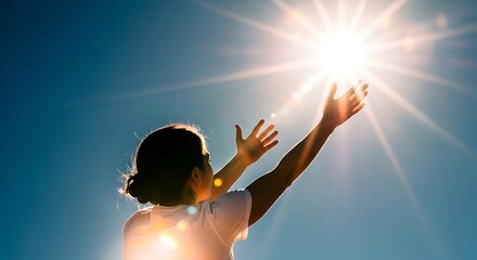 Woman reaching arms toward bright sunlight in blue sky.