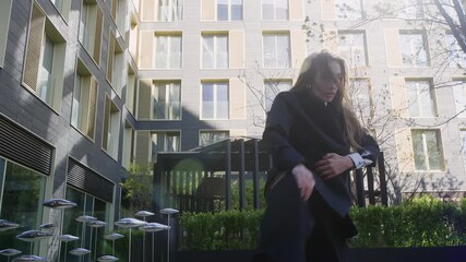Expressive dancer in modern black suit performs unique moves dancing contemporary modern dace in urban courtyard with greenery and metal sculptures, highlighting individuality and power.