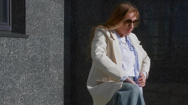 Flexible woman in light blazer and blue shirt dancing contemporary modern dace bends skillfully against urban wall, showing contemporary dance technique and emotion.