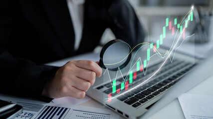 A business professional examines financial data on a laptop using a magnifying glass, highlighting stock market trends in a sleek office environment. Impute