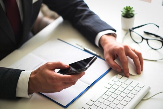 Businessman using smartphone and computer mouse at desk