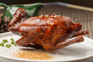 Crispy roasted pigeon, served on a round white porcelain plate, is placed on a placemat.