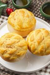A round white porcelain plate holds a pineapple bun with a crispy crust, placed on a placemat.
