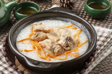 A black clay pot of cordyceps flower and pork rib congee was placed on a tablecloth.