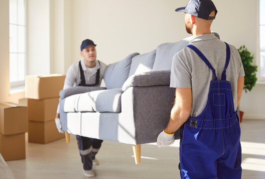 Two men movers carrying sofa from apartment, helping people to move to other place of living. Hard working workers from delivery service helping clients with relocation. Furniture delivery - Powered by Adobe